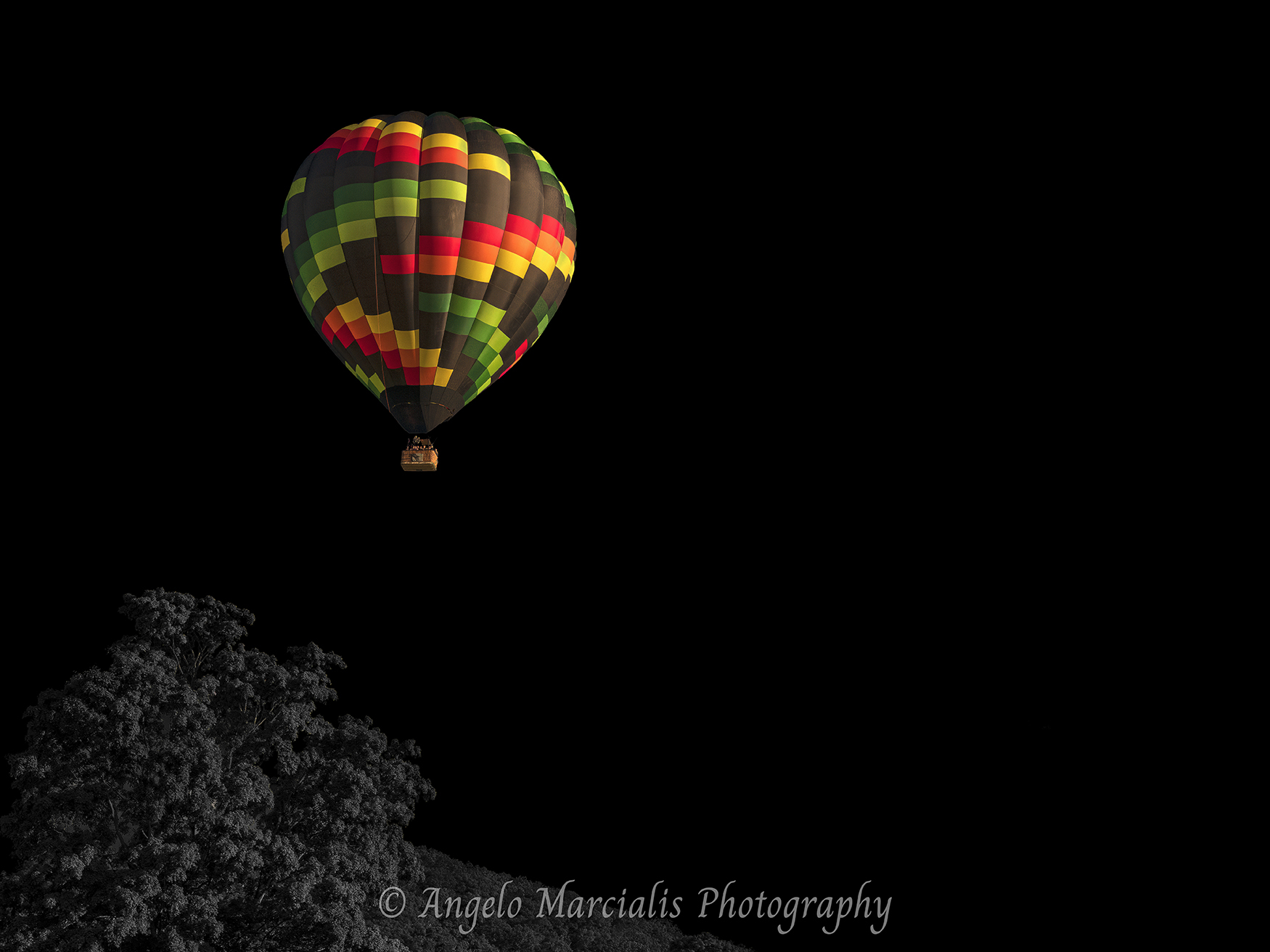 Multicolored hot air balloon soaring above a black-and-white landscape in the Hudson Valley, New York, combining vibrant color, dramatic contrast, and fine art landscape photography in a unique aerial scene.